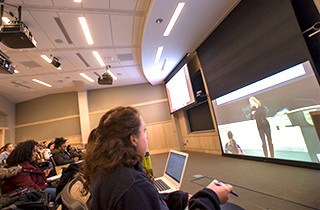 Students watching a professor speak on screen in a synchronous lecture hall at Rutgers-New Brunswick